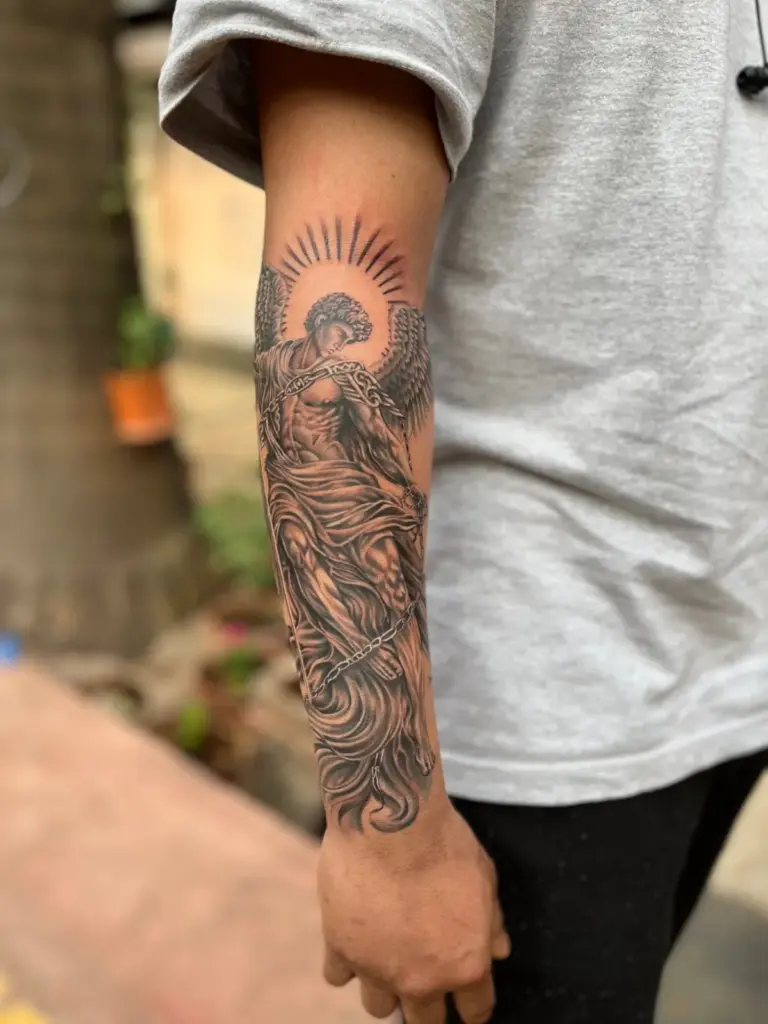 Black and grey realism angel with halo and chains tattoo on the forearm, Rays Tattoo Studio